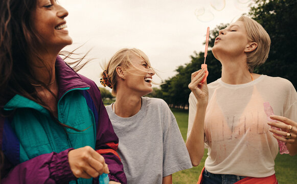 Three friends having fun outdoors, blowing bubbles and laughing happily