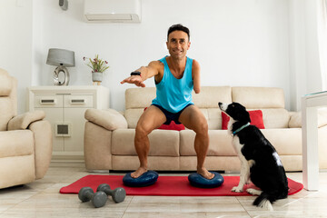 An adult man with an amputated arm exercises in his living room with his border collie dog. The...
