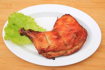 Roasted chicken leg on white plate against wood background.