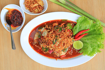 Oysters in spicy salad in white plate served with Chili Paste and fried onions against wood background.