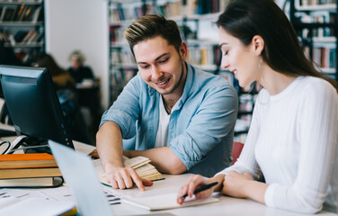 Smart students smiling while preparing with books and laptop in library