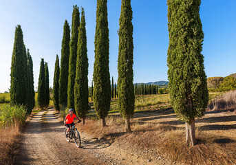 nice senior woman riding her electric mountain bike in a cypress avenue in the Ghianti Area of...