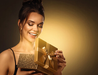 Gift giving for Woman. Beautiful Girl opening Present Box with shining Light. Happy smiling Model receive Surprise over Golden background - 666490851