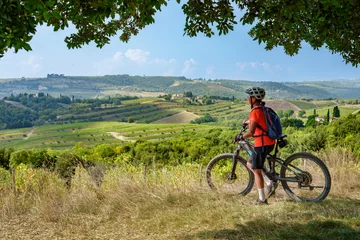 Foto auf Glas nice senior woman riding her electric mountain bike below a huge stone oak tree in the Ghianti Area of Tuscany, Italy © Uwe