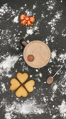 Black tablecloth full of flour, after having made homemade sweets for Christmas celebration. A mug of hot chocolate with a floating round chocolate, heart and lace cookies and a spoon with cocoa.