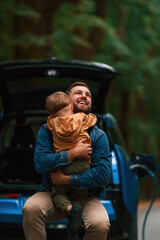 Father with his little son are waiting for electric car to charge © standret