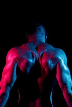 Shirtless muscular unrecognizable man in dark room with neon illumination