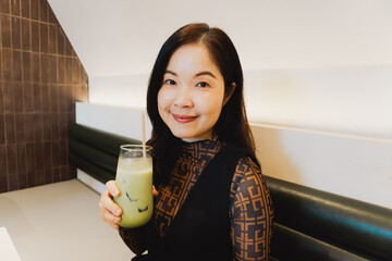 Asian woman with ice matcha in hand looking healthy at a cafe