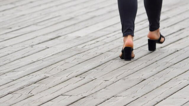 Close-up of a woman's feet in high heels on a wooden boardwalk.
