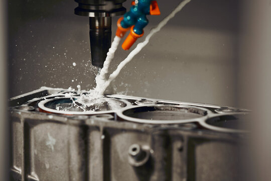 High precision cnc milling machine makes holes in the car engine with a coolant. 
