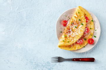An omelet with tomato and parsley, eggs for breakfast, a healthy vegetarian dish with cheese, shot from above on with a wooden fork and copy space - obrazy, fototapety, plakaty