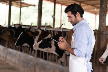 Portrait of white farmer man standing, holding record and writing data on paper with blur cow farm, Man farmer enjoy his lifestyle working at farm.