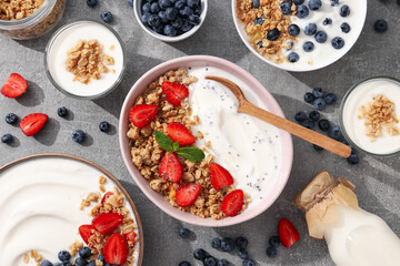 Bowls with yogurt and berries, wooden spoon and milk bottle on gray background, top view