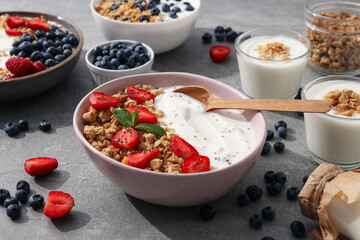 Bowls with yogurt and berries, wooden spoon and milk bottle on gray background
