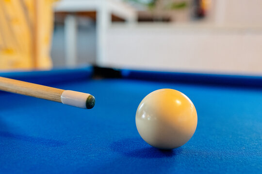 White billiard ball on blue pool table near cue