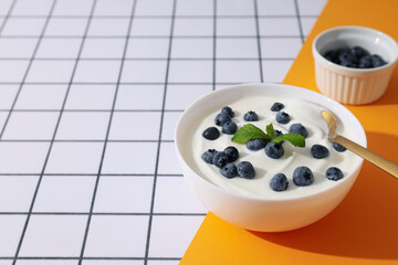 Bowls with yogurt and berries on white and yellow background, space for text