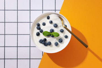 Bowl with yogurt and berries, spoon on white and yellow background, top view