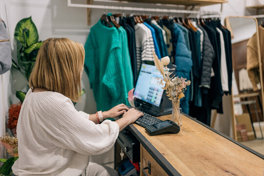 Boutique employee woman manages tasks on computer in a counter amidst clothing.