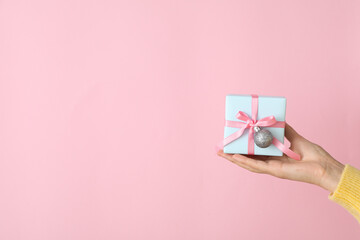 Gift box in female hand on pink background, space for text