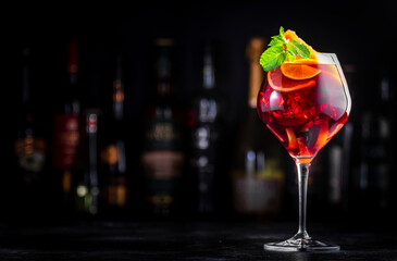 Red sangria cocktail drink with tempranillo wine, peach, plum, orange, lime and ice. Black bar counter background, steel bar tools and bottles