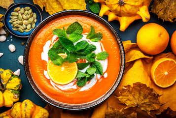 Sweet autumn pumpkin soup with cream, tangerine and mint. Winter healthy vegetarian comfort slow food. Soup bowl on green table background. Top view