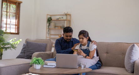 Fototapeta na wymiar Young indian couple stress using laptop and credit card for shopping online internet payment buying from internet and sitting at home