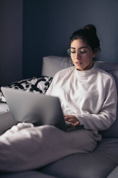 Positive young woman resting on sofa on laptop at home