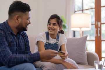 Indian couple shopping online with laptop and credit card from home, sitting on sofa in living room