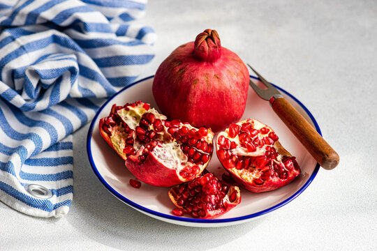 Open ripe pomegranate on plate with a rustic knife and a striped napkin.