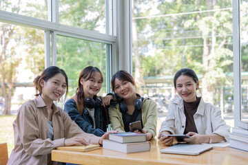 University students sitting together at table with book and laptop. Happy young people doing group study in college campus