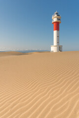 Lighthouse of Delta del Ebro among the Fangar beach dunes at sunset in a sunny day