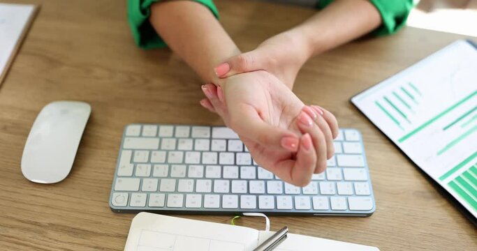 A young woman in the office massages her wrist, hands close-up. Pain in the hand at work, office disease