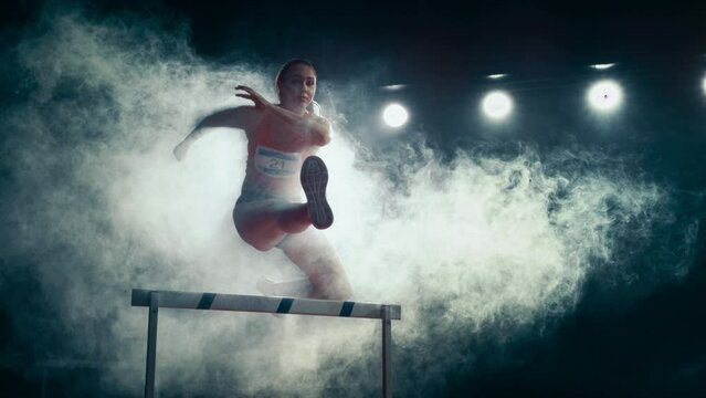 Strong Female Athlete is Running Towards an Obstacle, Jumping Over the Barrier at High Speed while Sprinting. Cinematic Dark Studio Sports Footage with Super Slow Motion Speed Ramp and Smoke Effects