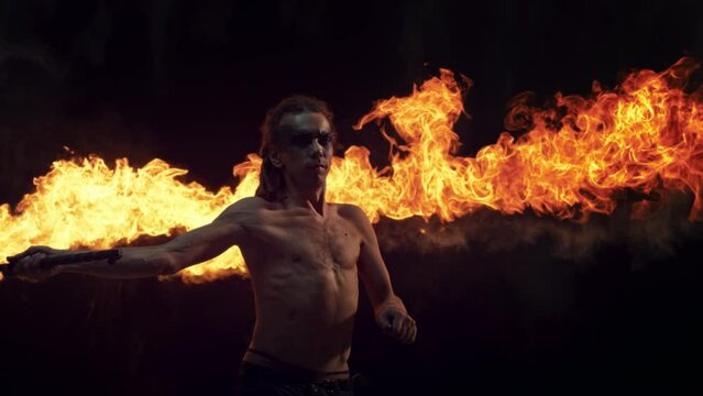 Fire Artist Performing at a Show on a Dark Stage. Male Performer Spinning with a Fire Torch with Beautiful Visual Effect. Cinematic Super Slow Motion Footage with Speed Ramp Effect