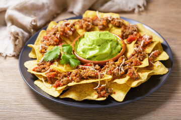 Plate of mexican nachos chips with cheese, meat and guacamole