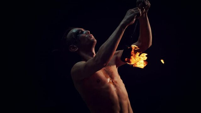 Eccentric Fire Performer Spinning Fire Pois at a Show. Male Artist Juggling Fire Balls in a Dramatic Live Performance in Low Key Light. Aesthetic Super Slow Motion Footage with Speed Ramp Effect