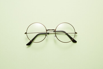 Glasses in round thin metal frame isolated on light green surface.