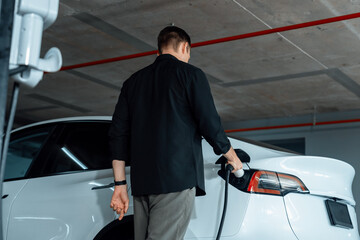Young man travel with EV electric car to shopping center parking lot charging in downtown city...