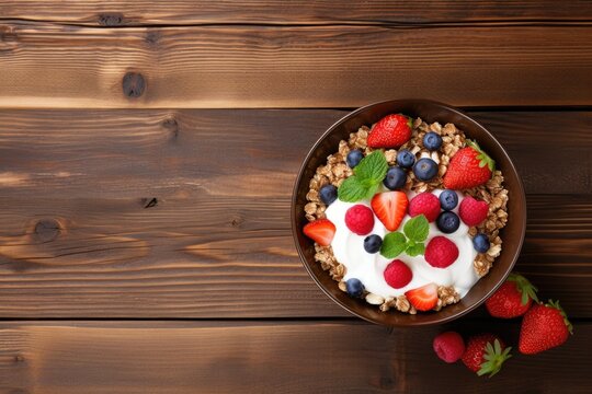 Homemade granola bowl with yogurt and berries on wooden surface seen from above