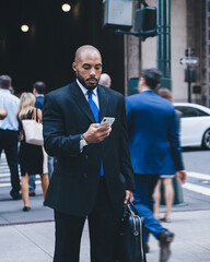 Black businessman walking with smartphone