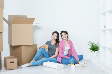 Girlfriends moving to a new apartment sit on the floor with a plan of the house,