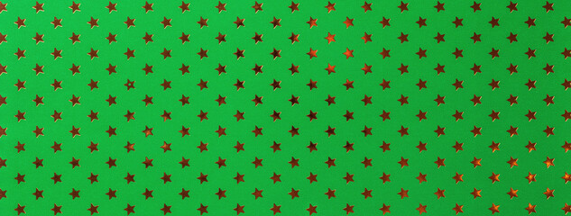 Dark green background from metal foil paper with pattern of golden stars. Texture of metallized backdrop.