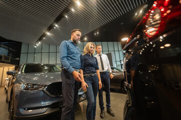 The seller demonstrates the interior of the car to buyers. Caucasian couple chooses a car.