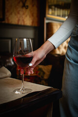 Hand holding a glass of red wine in a cozy bar setting