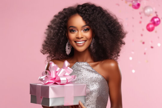 Beautiful African American Girl Holding Gift Box In Her Hands. Pretty Curly Hair Woman Posing With Xmas Present In Her Arms, Pink Studio Background