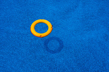 Top view of lifebuoy floating in blue swimming pool, soft focus.