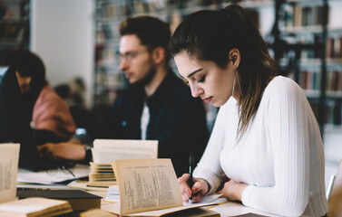 Focused lady writing memo in notepad in library
