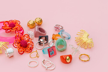 Colorful trendy bijouterie on pink background. Fashion silver, golden and plastic, acrylic and ceramic rings, bracelets and earrings. Stylish accessories. Women's jewelry.