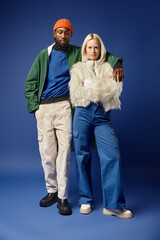 young woman and african american man in winter attire, diverse models standing on blue backdrop