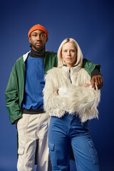 african american man hugging blonde woman in winter attire, diverse models standing on blue backdrop